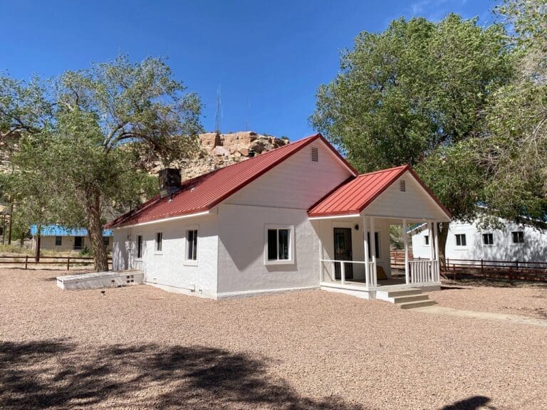 Remodeled single-story home with white exterior, red metal roof, front porch entry, and gravel yard in a desert setting.