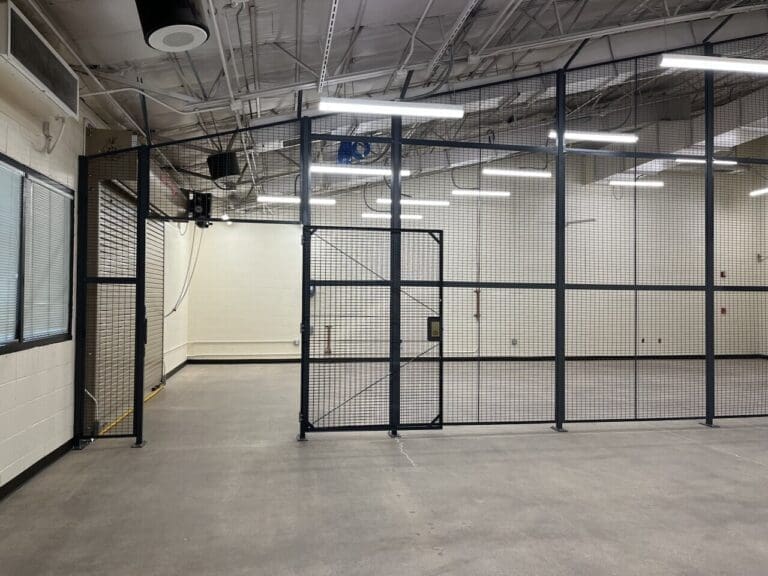 Interior build-out at Sky Harbor Airport featuring a large black metal mesh security enclosure with gate, overhead lighting, and finished concrete flooring