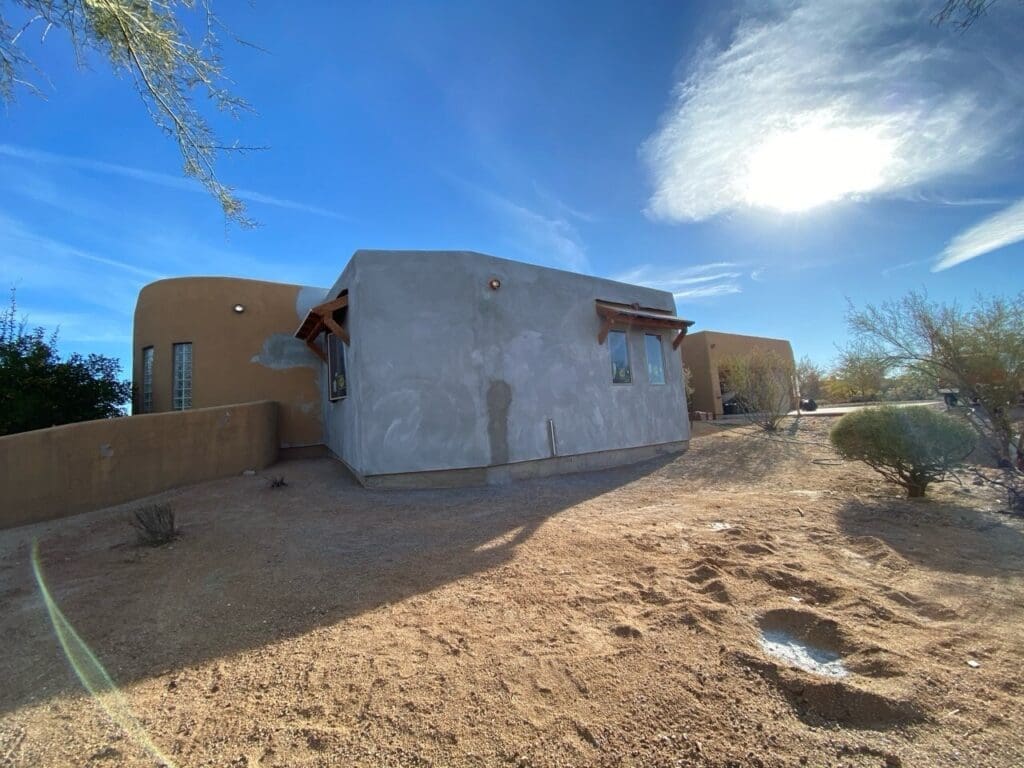 Exterior view of a newly stuccoed home addition with desert landscaping and bright sunlight in the background