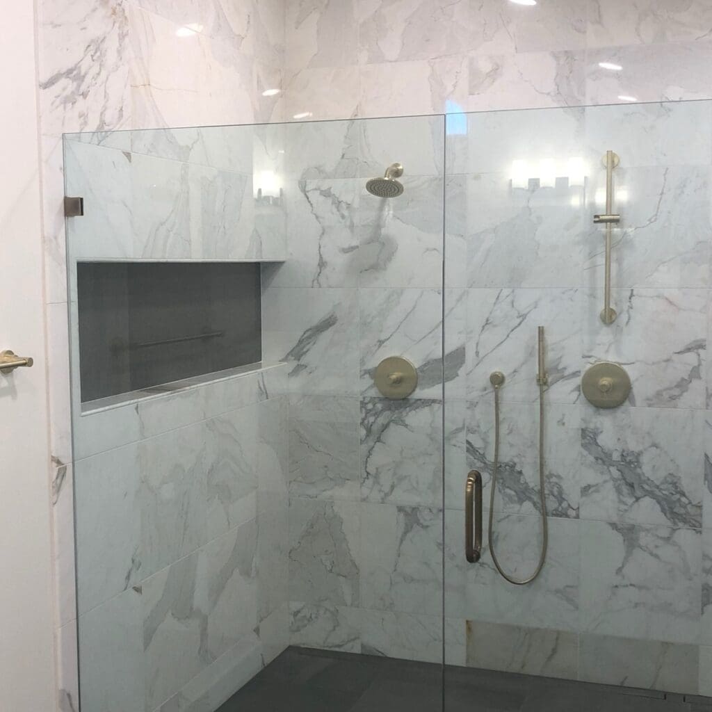 Modern walk-in shower with full-height marble tile walls, built-in niche, gold fixtures, and frameless glass door.