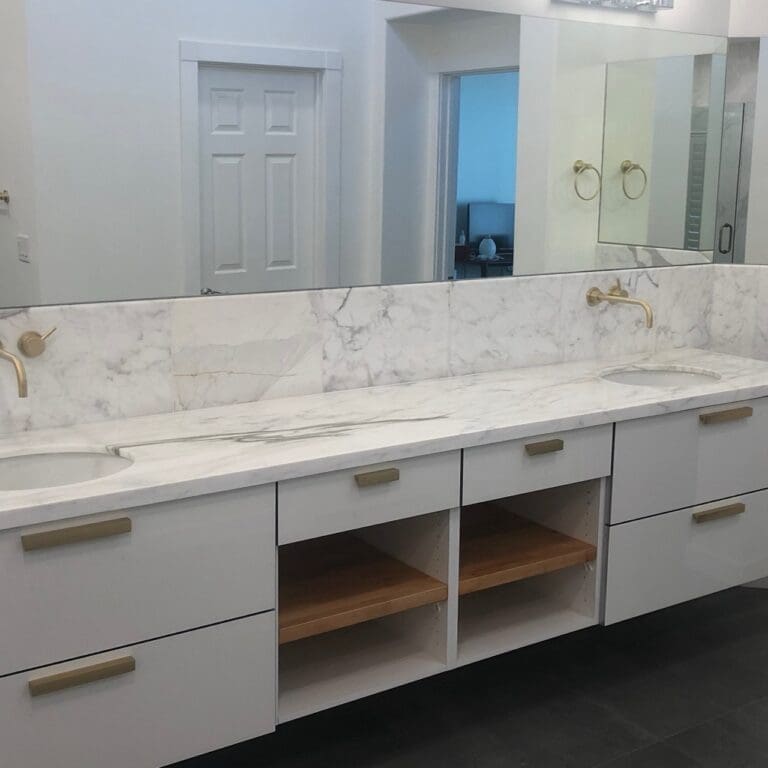 White floating bathroom vanity with marble backsplash, wall-mounted gold faucet, and integrated mirror cabinet
