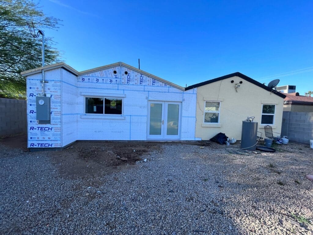Exterior view of a house under construction with new R-Tech insulation installed on the addition and freshly installed patio doors.