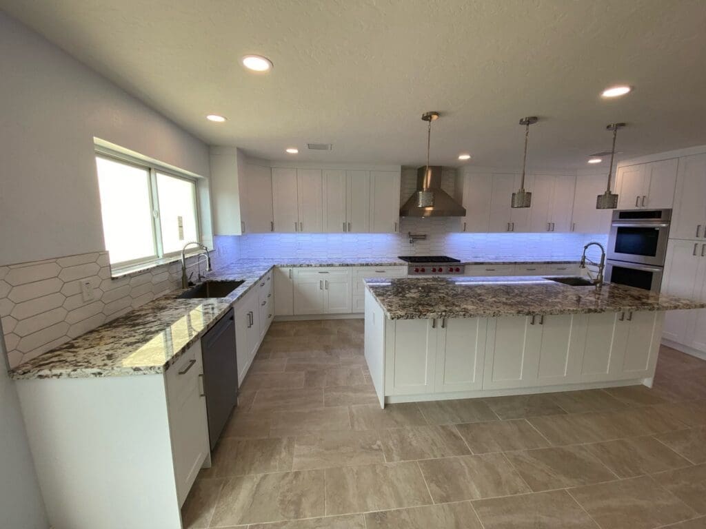 Wide angle of modern kitchen with white cabinetry, granite counters, and tile flooring