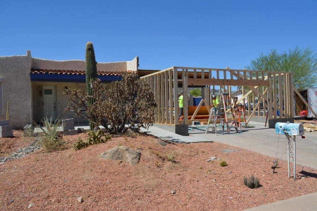 Stuccoed exterior patio enclosure under construction with new grey walls, exposed roof trim, and a door leaning against the wall.