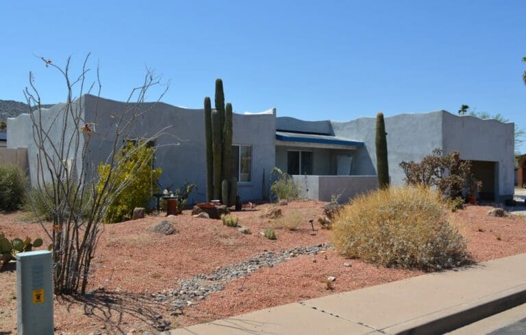Front view of a Southwestern-style stucco home with desert landscaping, mature cacti, and a completed garage and porch addition.