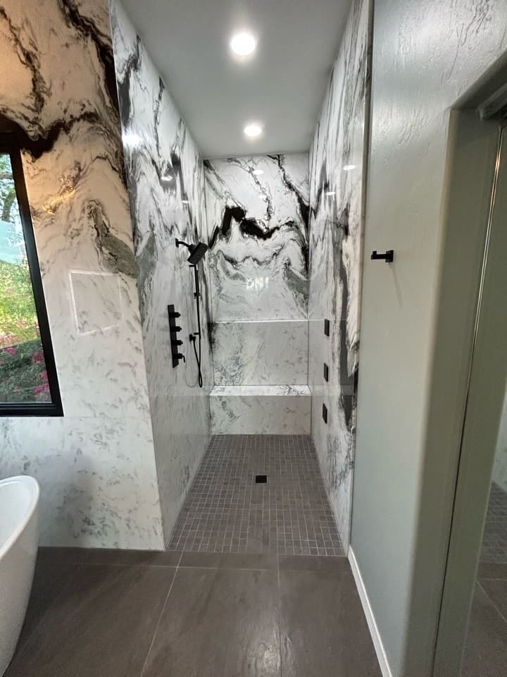 Modern walk-in shower with marble-patterned walls, recessed lighting, a built-in bench, and matte black fixtures
