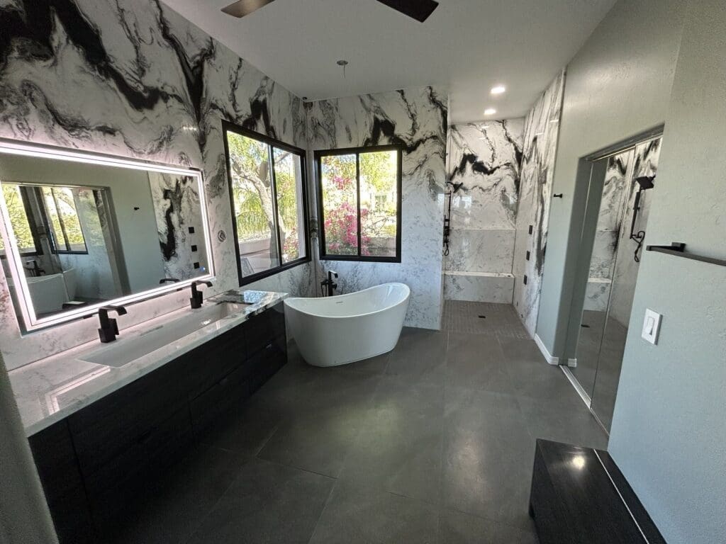 Spacious modern bathroom with a freestanding tub by large windows, a marble-accent vanity with a backlit mirror, and a walk-in shower featuring dramatic black-and-white stone walls.