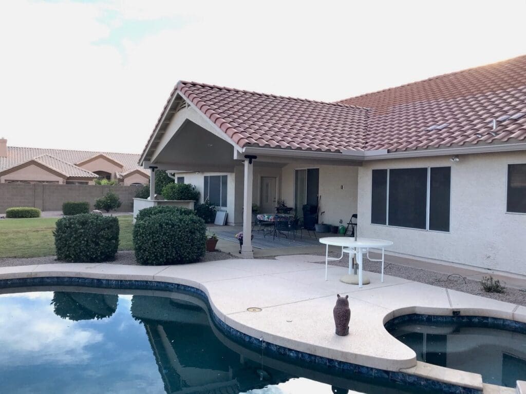 Completed Scottsdale backyard patio with new gable roof, covered seating area and pool deck overlooking the landscaped yard at sunset.