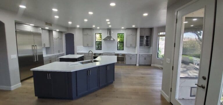 A modern, spacious kitchen with a large island, white cabinetry, stainless steel appliances, and recessed ceiling lights